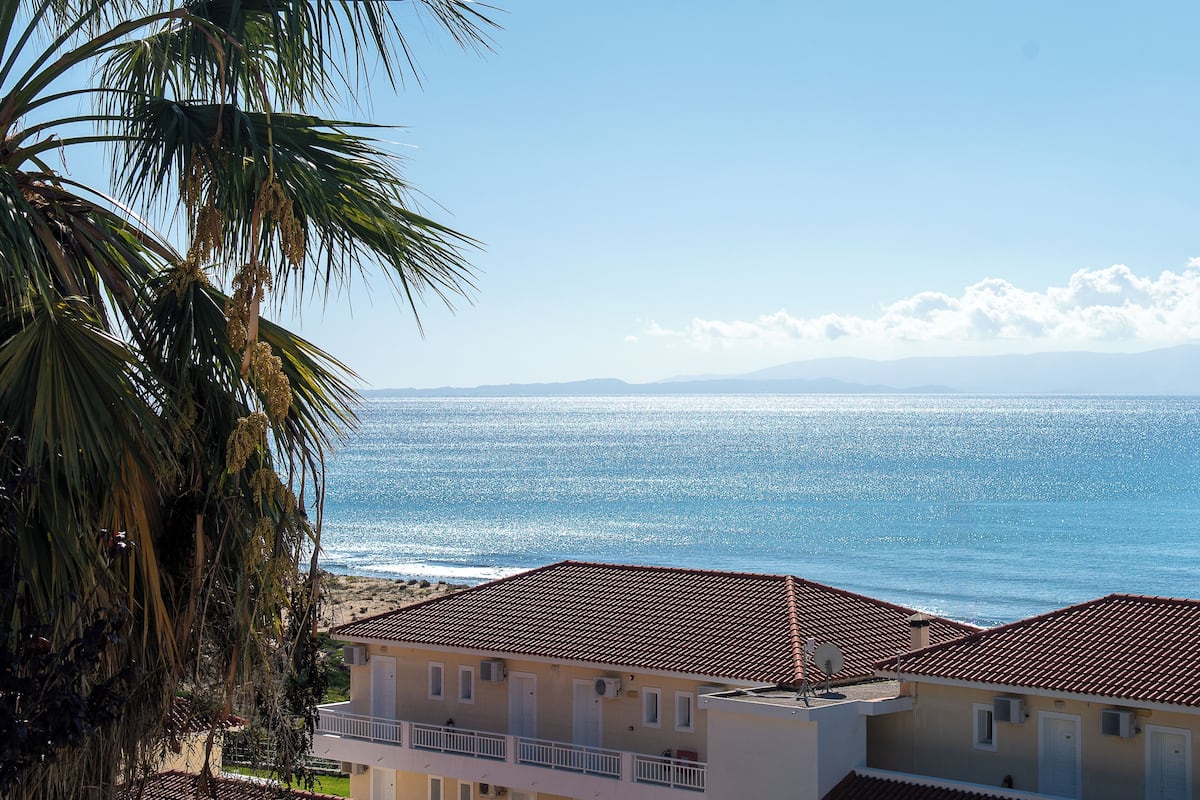 A coastal building with a red-tiled roof, a balcony, and a view of the sea.