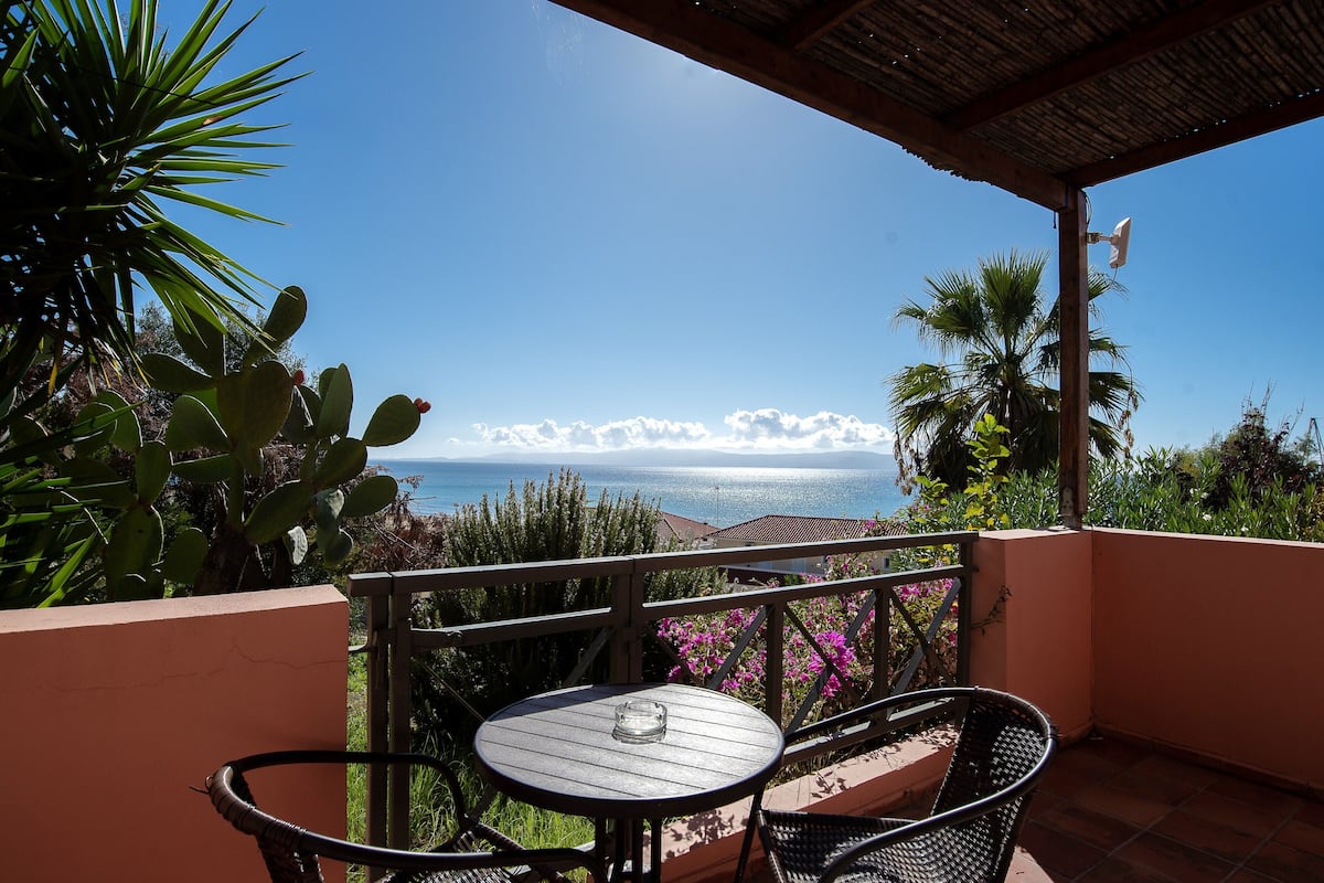 A balcony with a table and chairs, overlooking a coastal view with the sea and clouds.