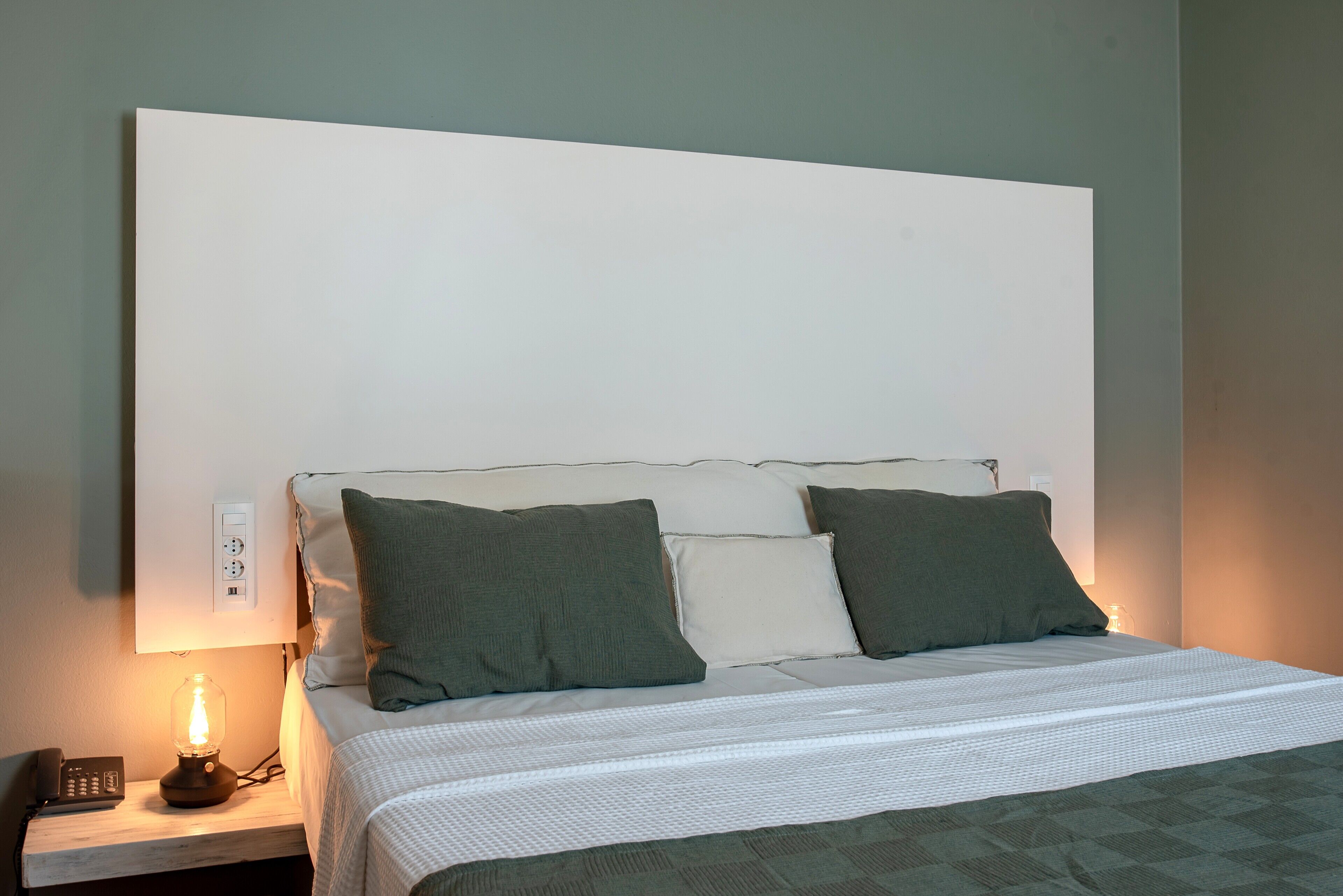 Un lit bien fait, avec une tête de lit blanche, deux oreillers et une lampe de chevet.