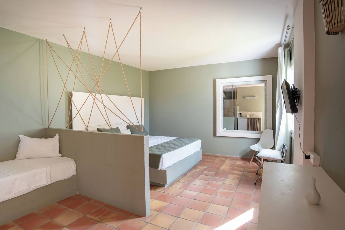 A bedroom with a bed, a desk, and a chair. There is a window with curtains and a mirror on the wall.