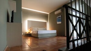 A bedroom with a bed, bedside table, and a nightstand. There is a window with curtains, a wall-mounted air conditioner, and a painting on the wall. - Mounda Beach Retreat (Skala)
