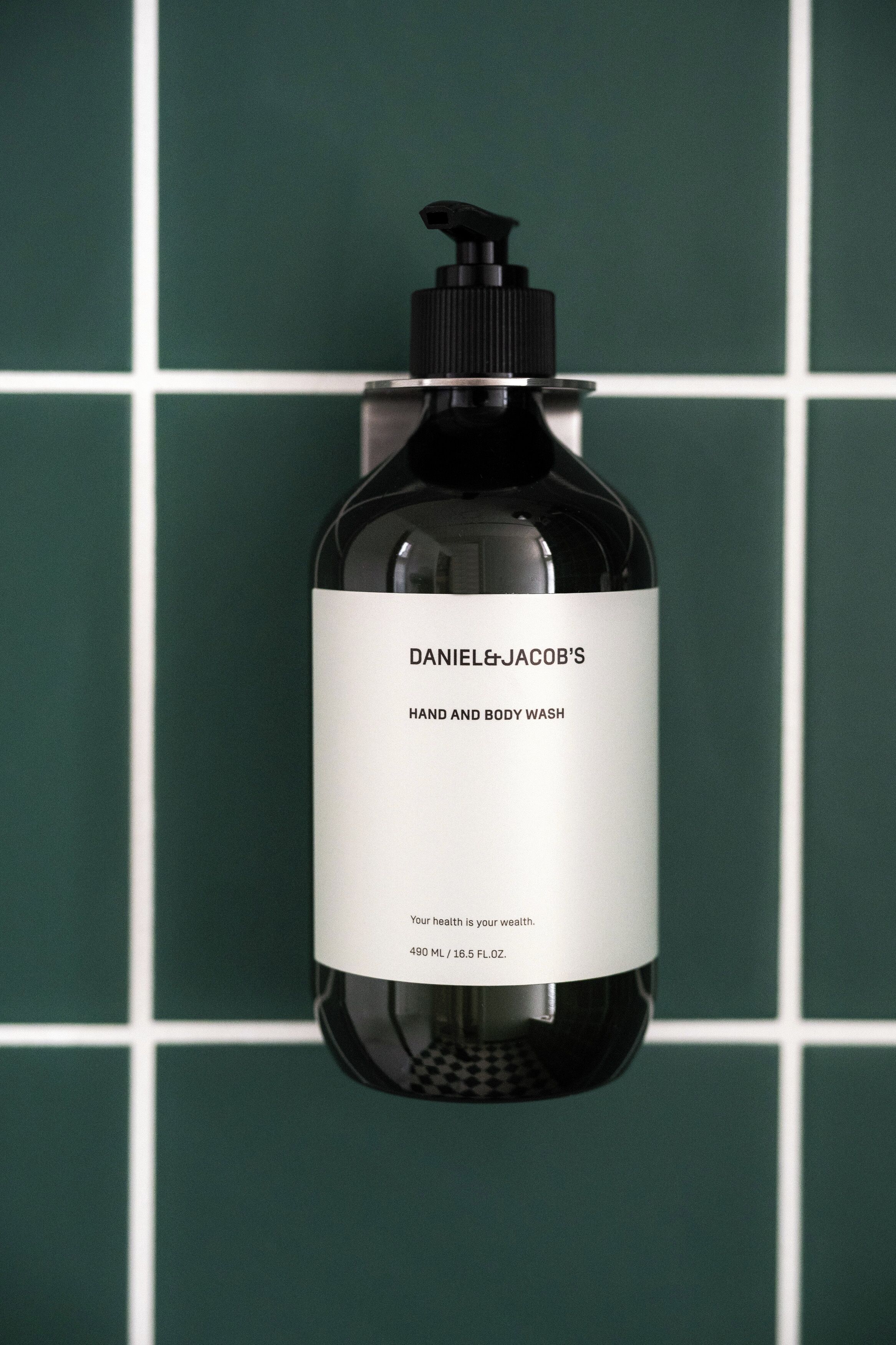 A bottle of Daniel & Jacob's Hand and Body Wash against a green tiled wall.