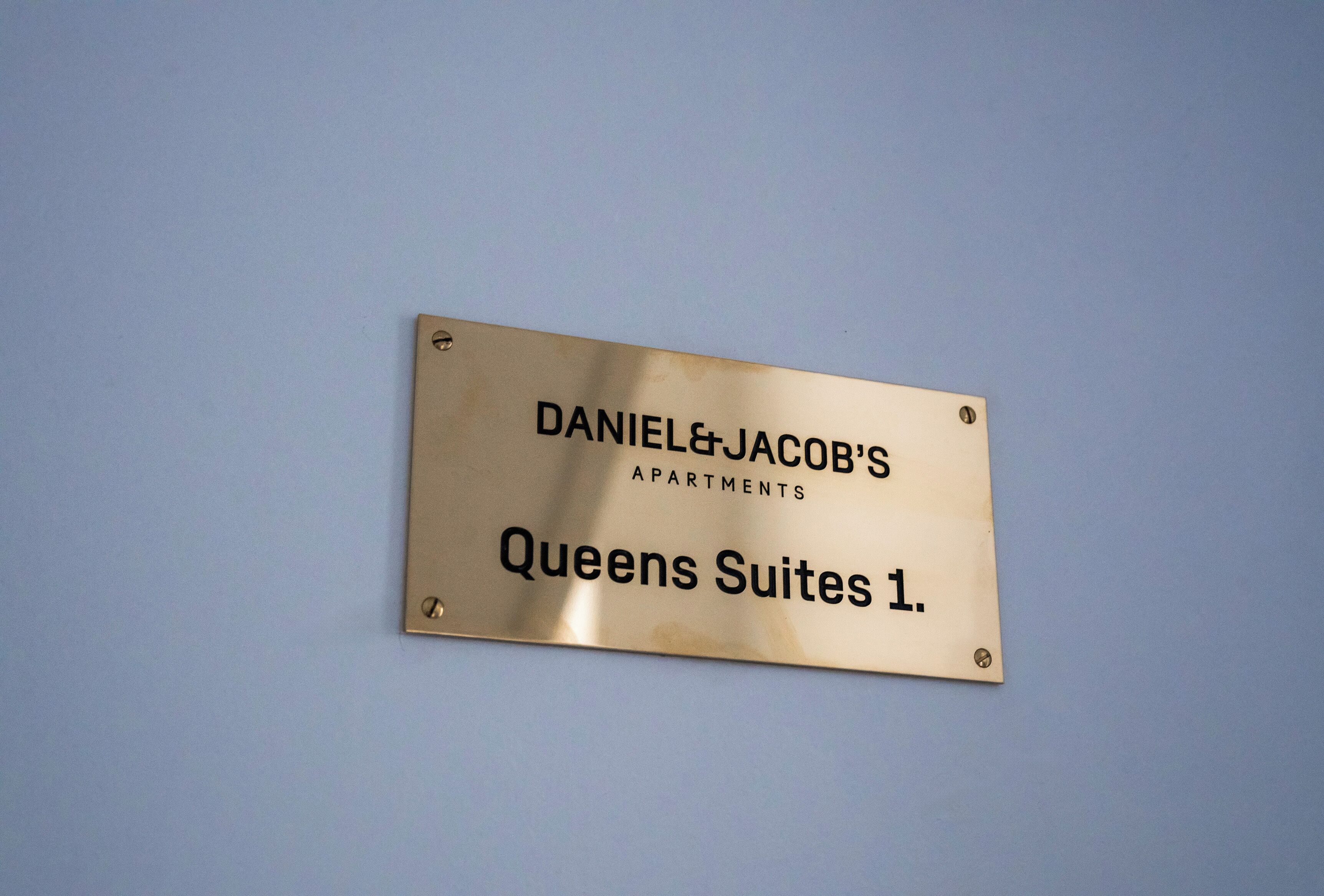 A brass plaque with text indicating it is for Queens Suites 1 at Daniel & Jacob's Apartments.