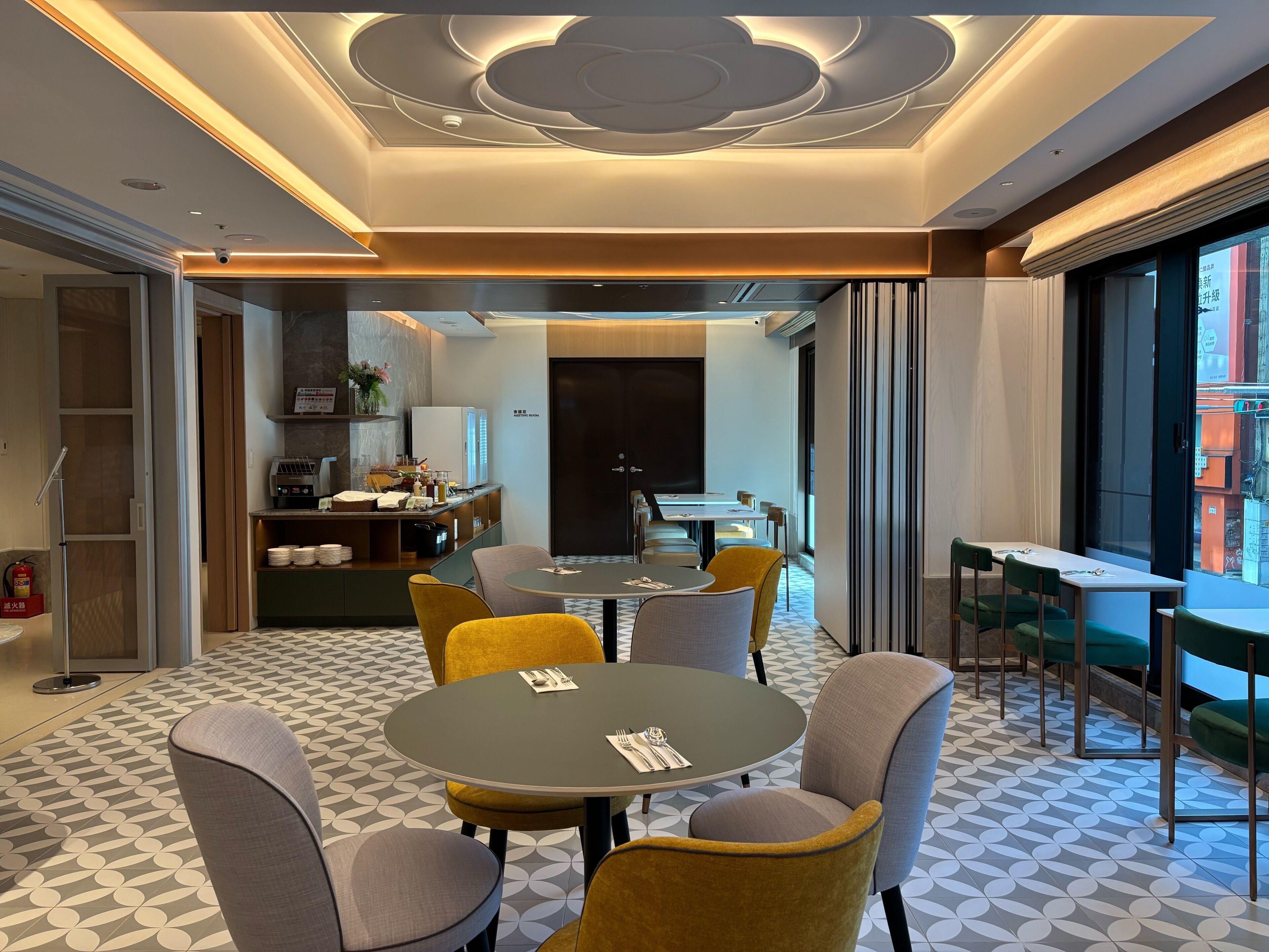 A modern hotel lobby with a dining area, a reception desk, and a view of the city.