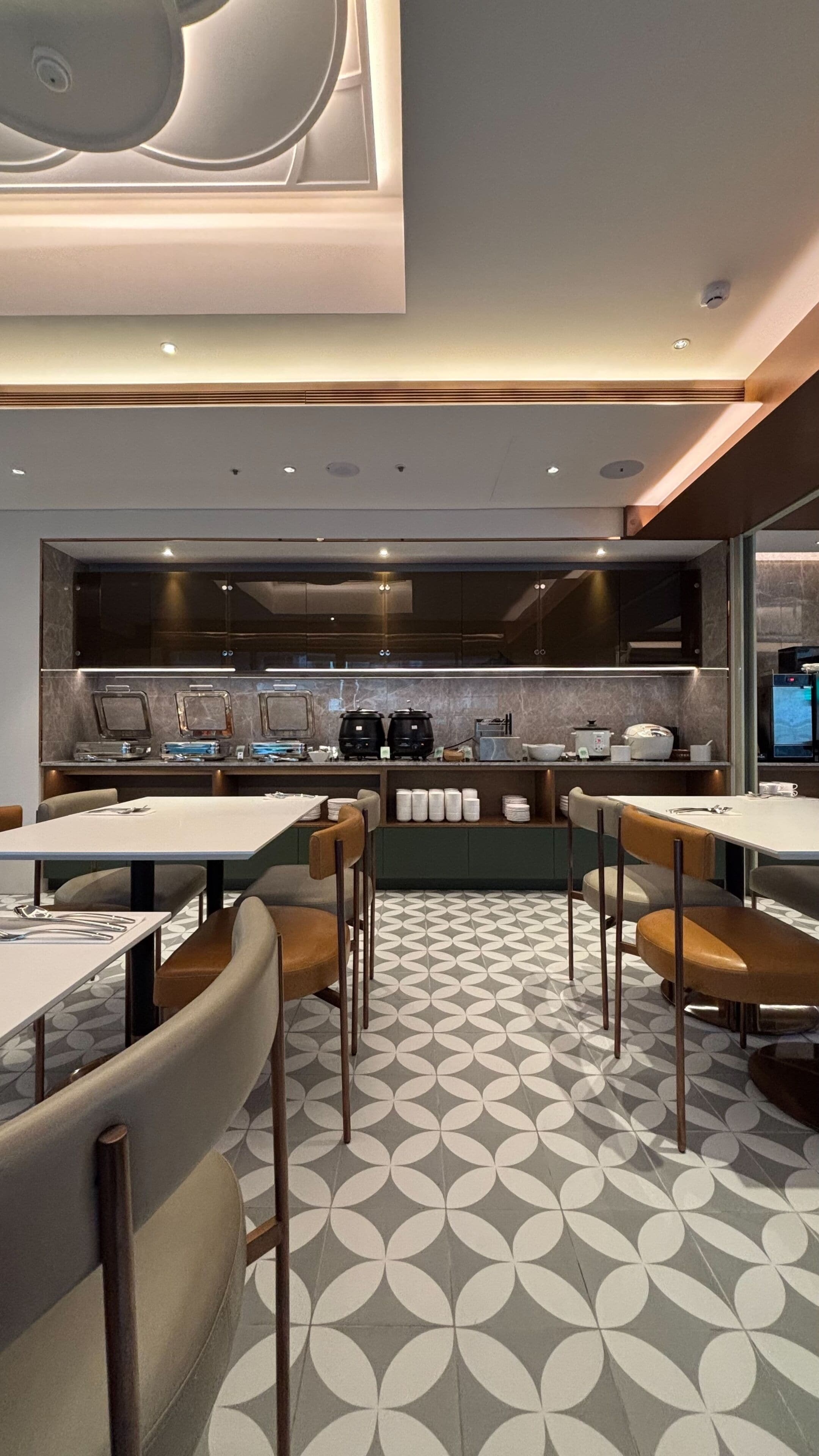 A modern restaurant with a central bar area, seating with high backs, and a patterned floor.