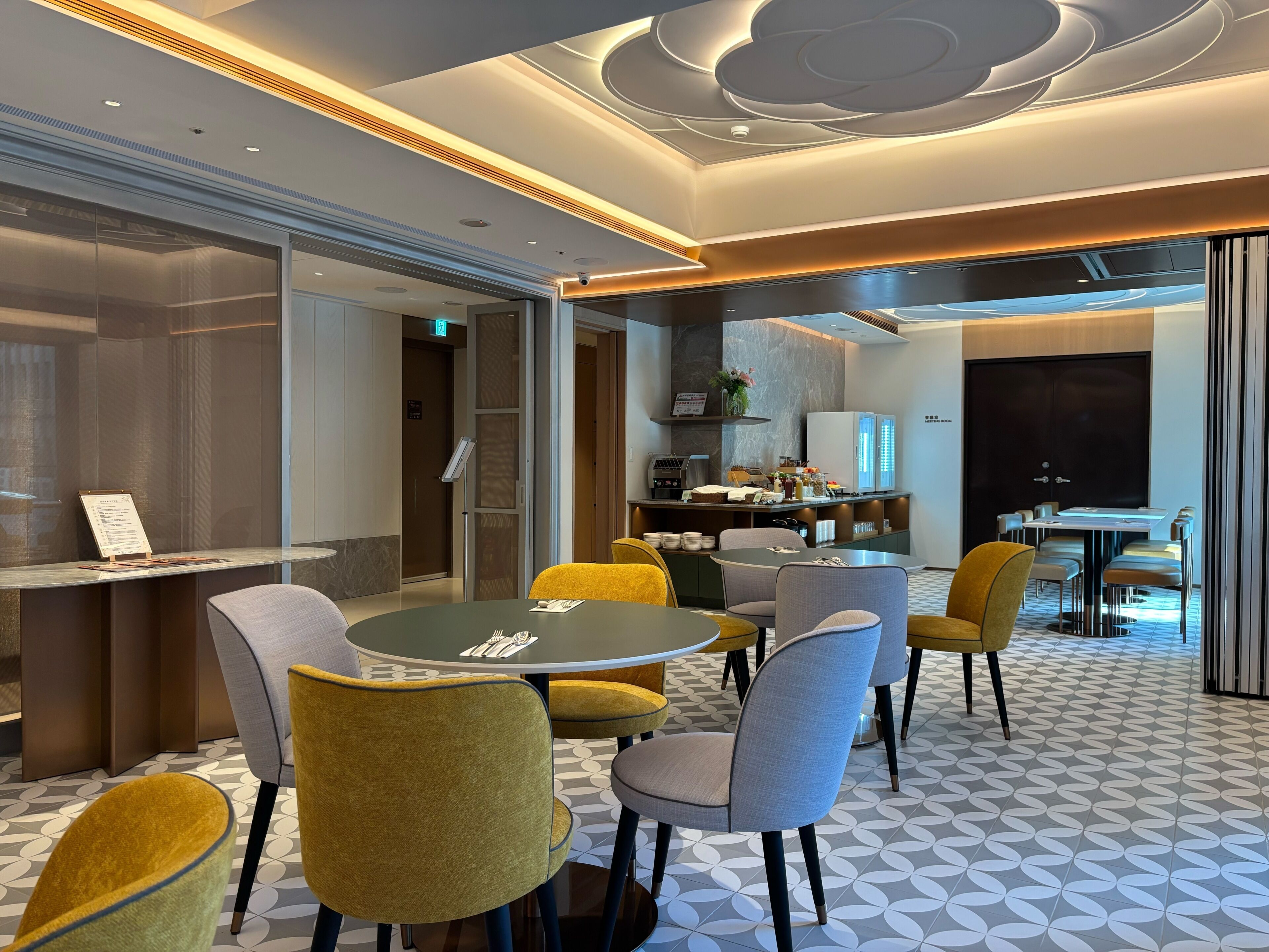 A modern hotel lobby with a reception desk, seating area, and a kitchenette.