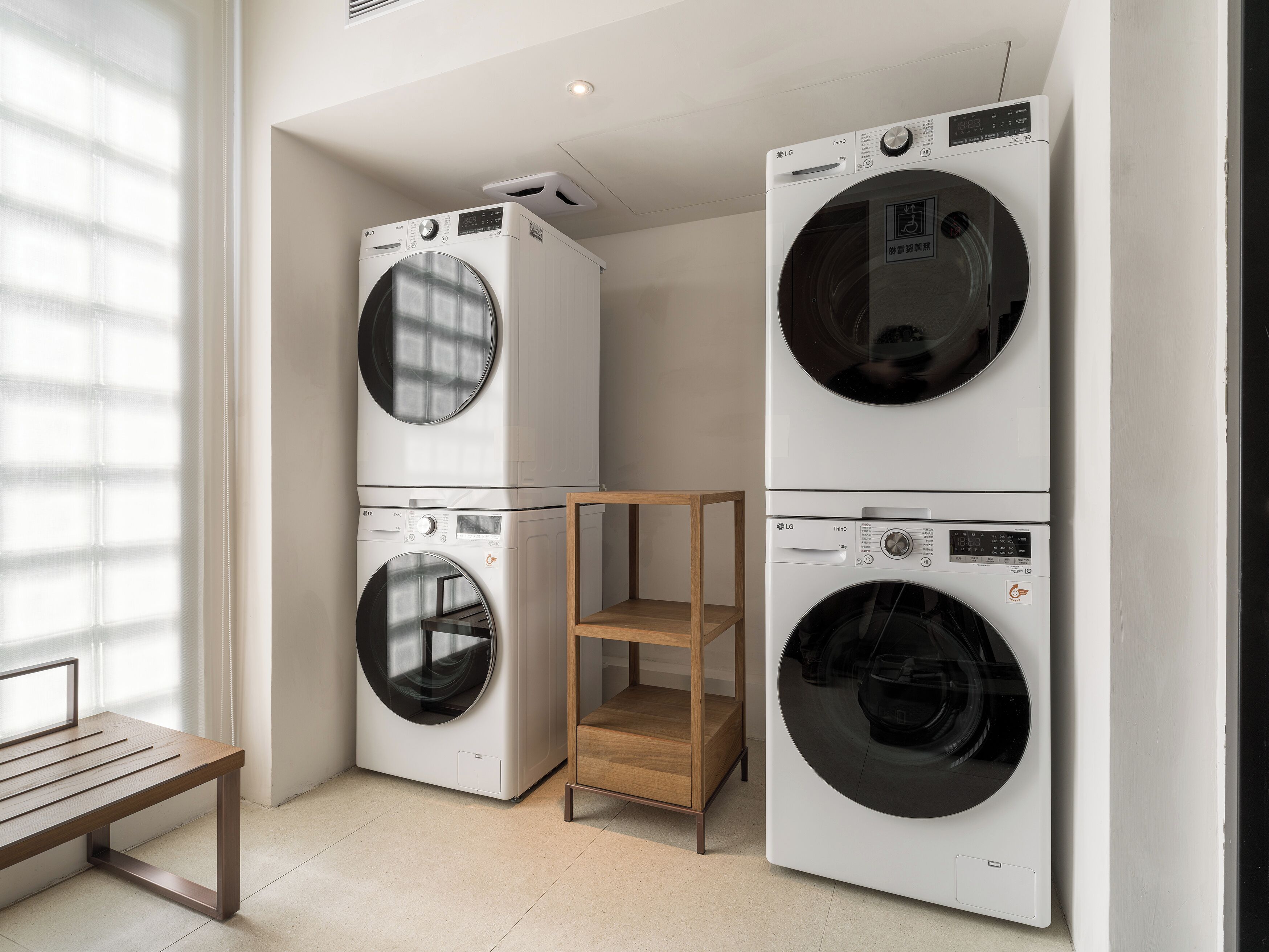 A laundry room with stacked washing machines, a wooden bench, and a shelf unit.