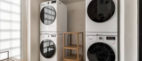 A laundry room with stacked washing machines, a wooden bench, and a shelf unit.