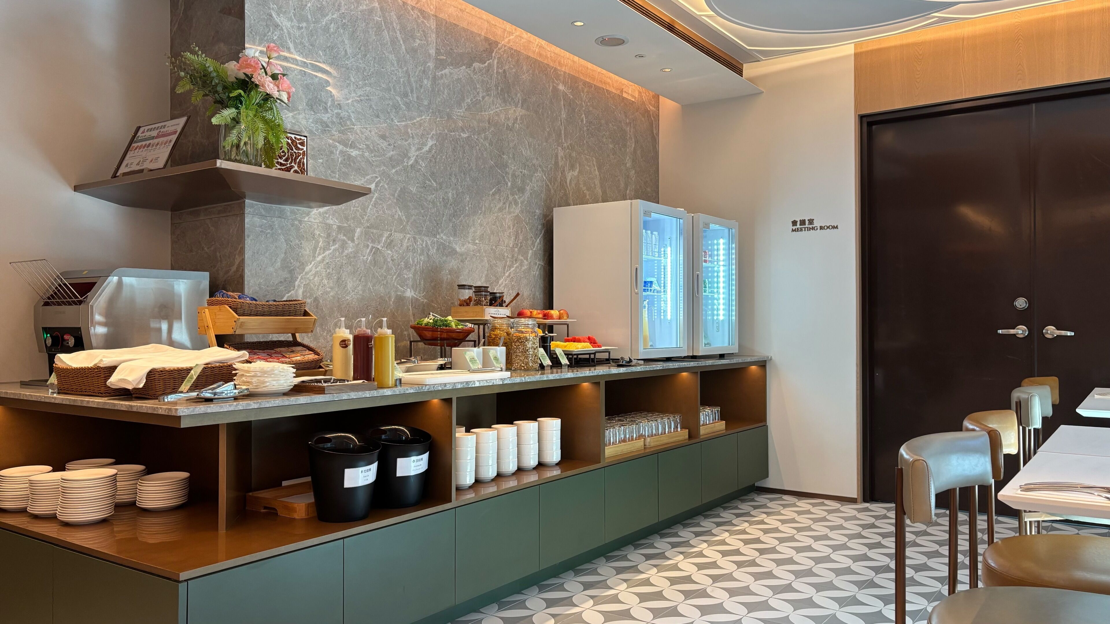 A modern breakfast bar with a marble backsplash, a meeting room sign, and a view of the cityscape through the glass doors.