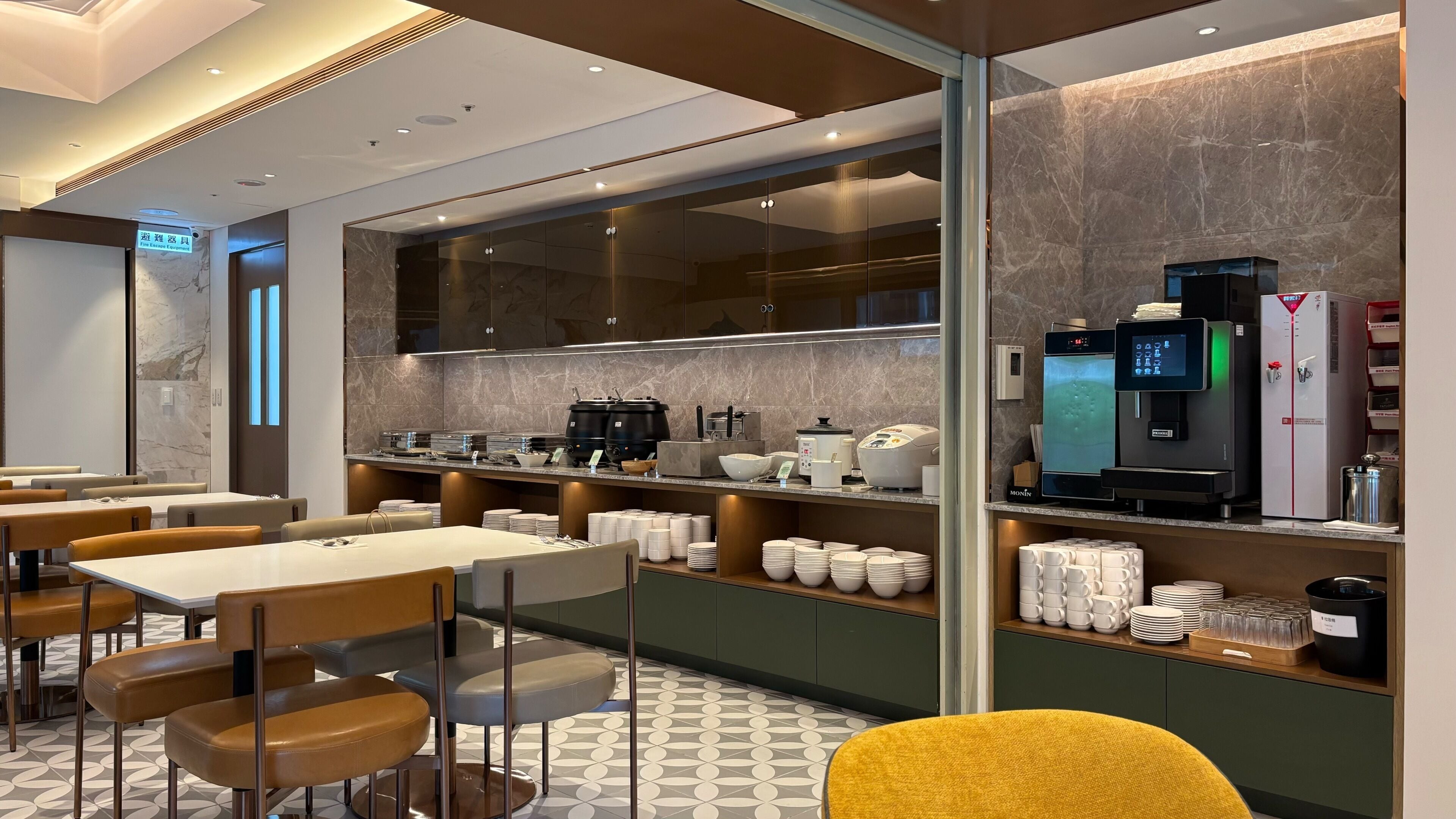 Una habitación de hotel moderna con zona de comedor, cocina equipada con cafeteras y un minibar.