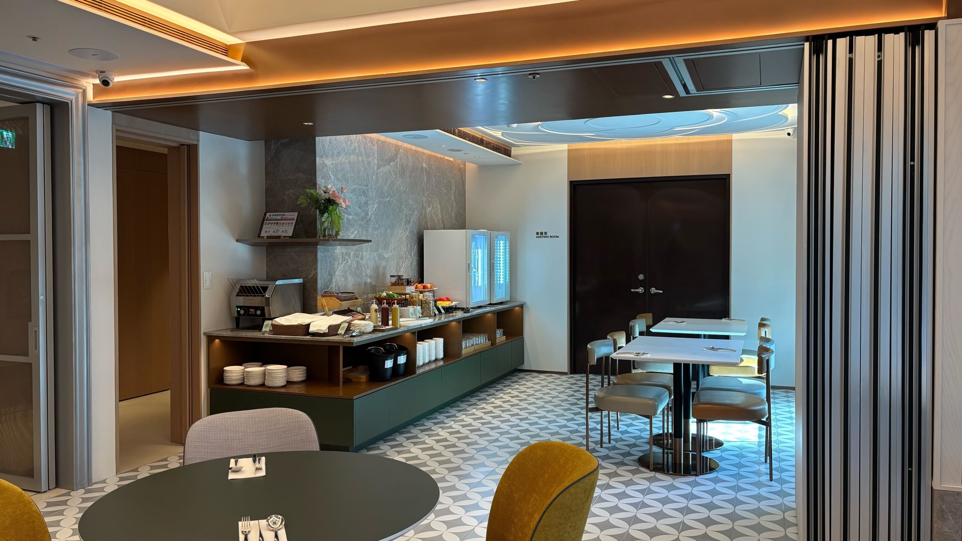 A modern dining area with a buffet setup, a seating arrangement, and a door labeled 'ASSISTING ROOM'.