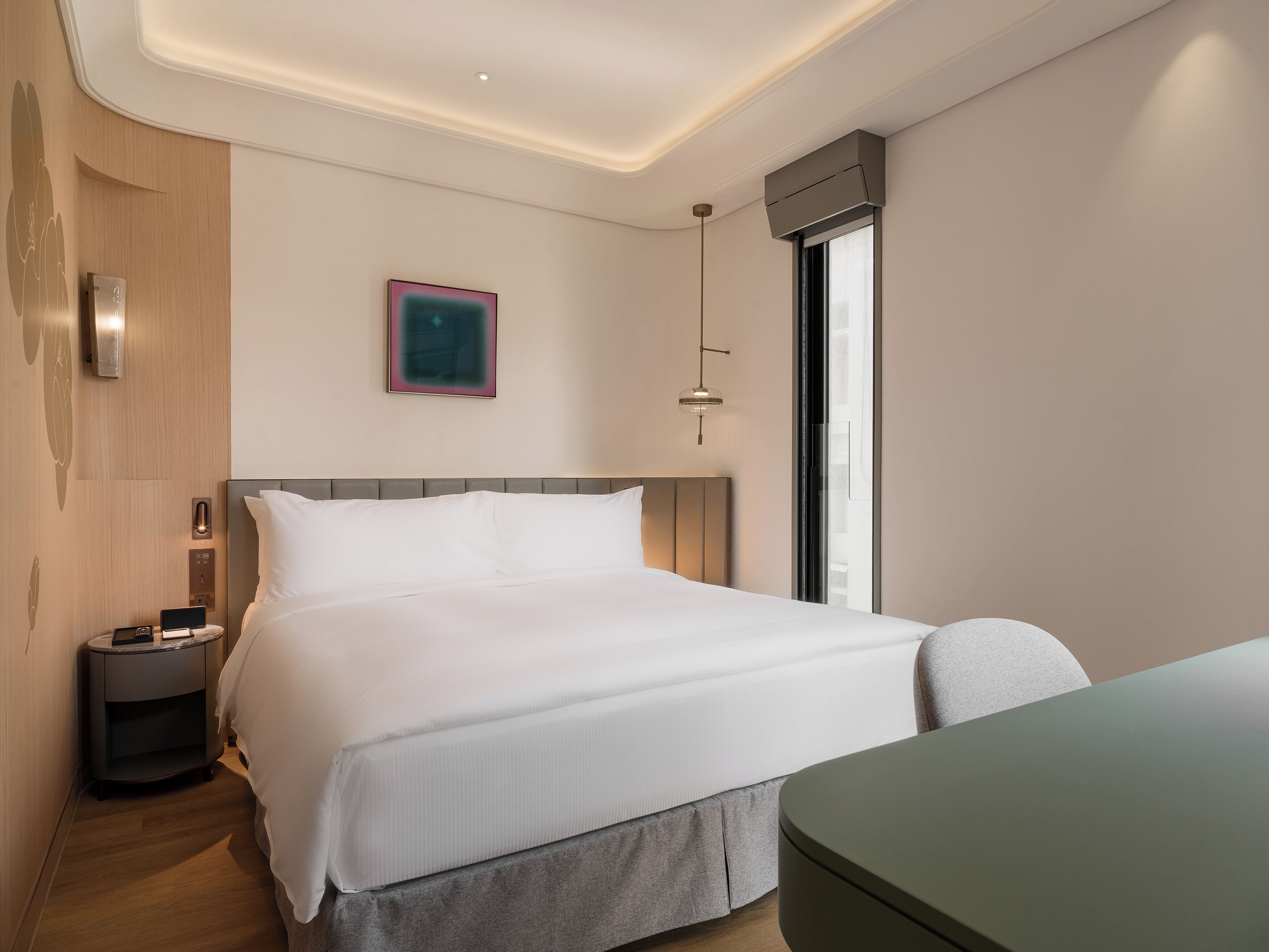 A modern hotel room with a large bed, bedside tables, a desk, and a window.