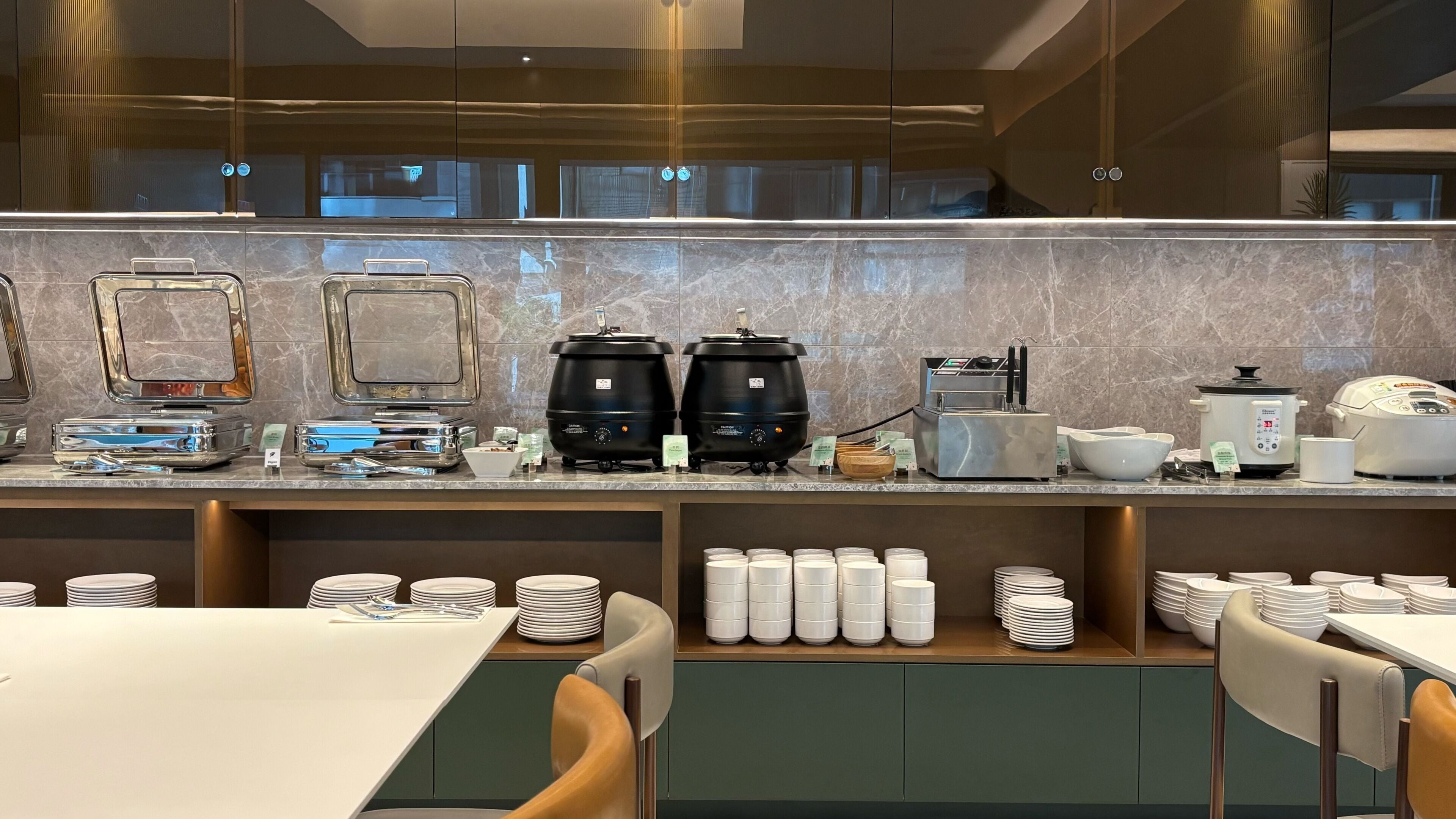 A modern kitchen area with a marble countertop, coffee machines, a rice cooker, and neatly stacked plates and bowls.