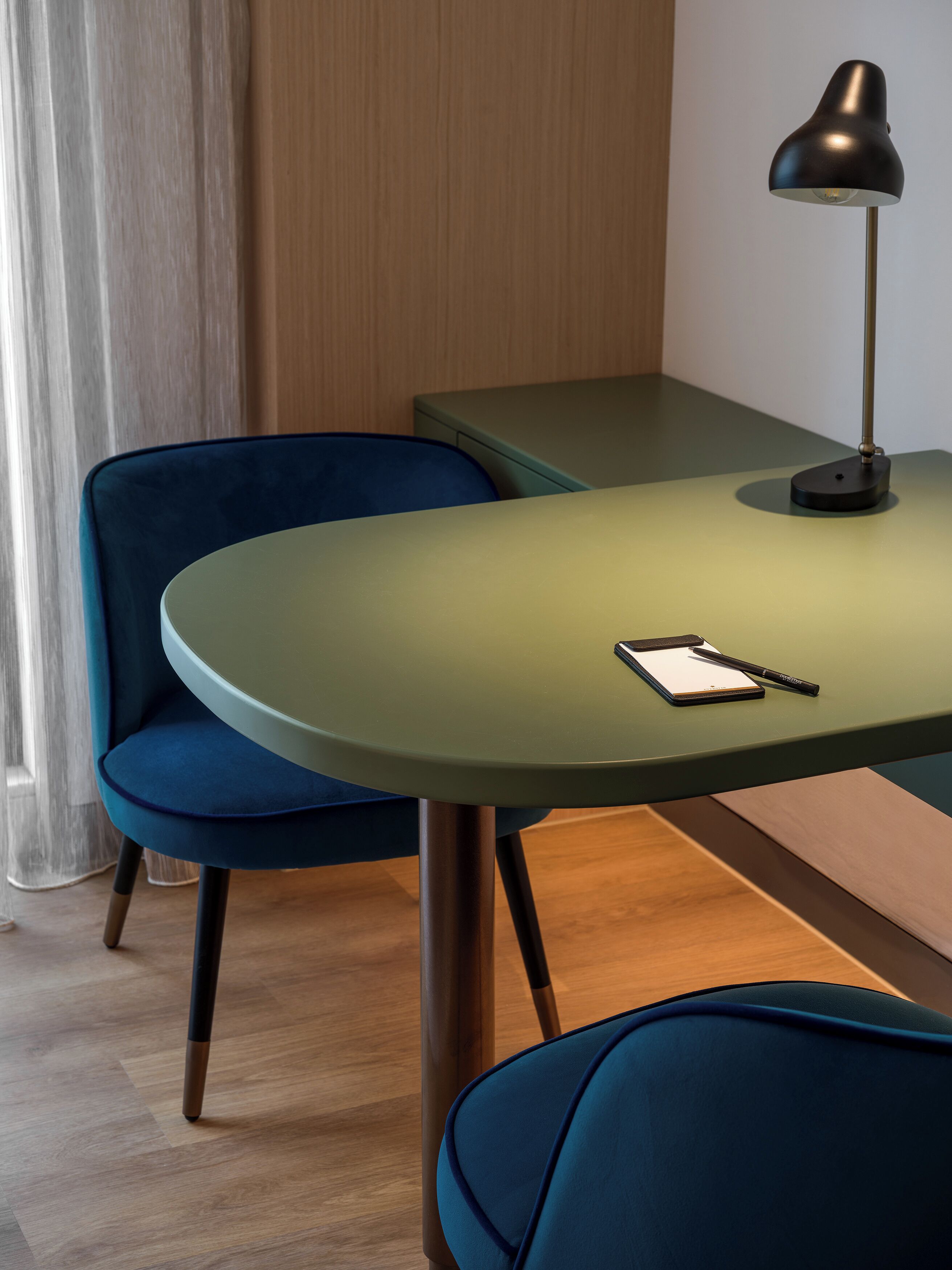 Une pièce moderne avec une table verte, une chaise bleue et une lampe de bureau.