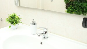 A bathroom with a white sink, a mirror, a small potted plant, and a green wall decoration. - GOCCE DI LUNA (San Lucido)