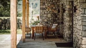 Une terrasse couverte avec des murs en pierre, une table en bois, des chaises en osier et une plante en pot.