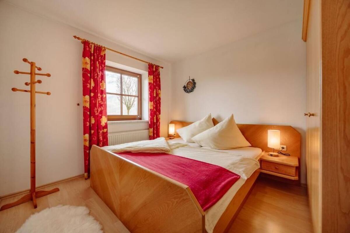 A bedroom with a wooden bed, red curtains, a bedside table with a lamp, and a radiator.