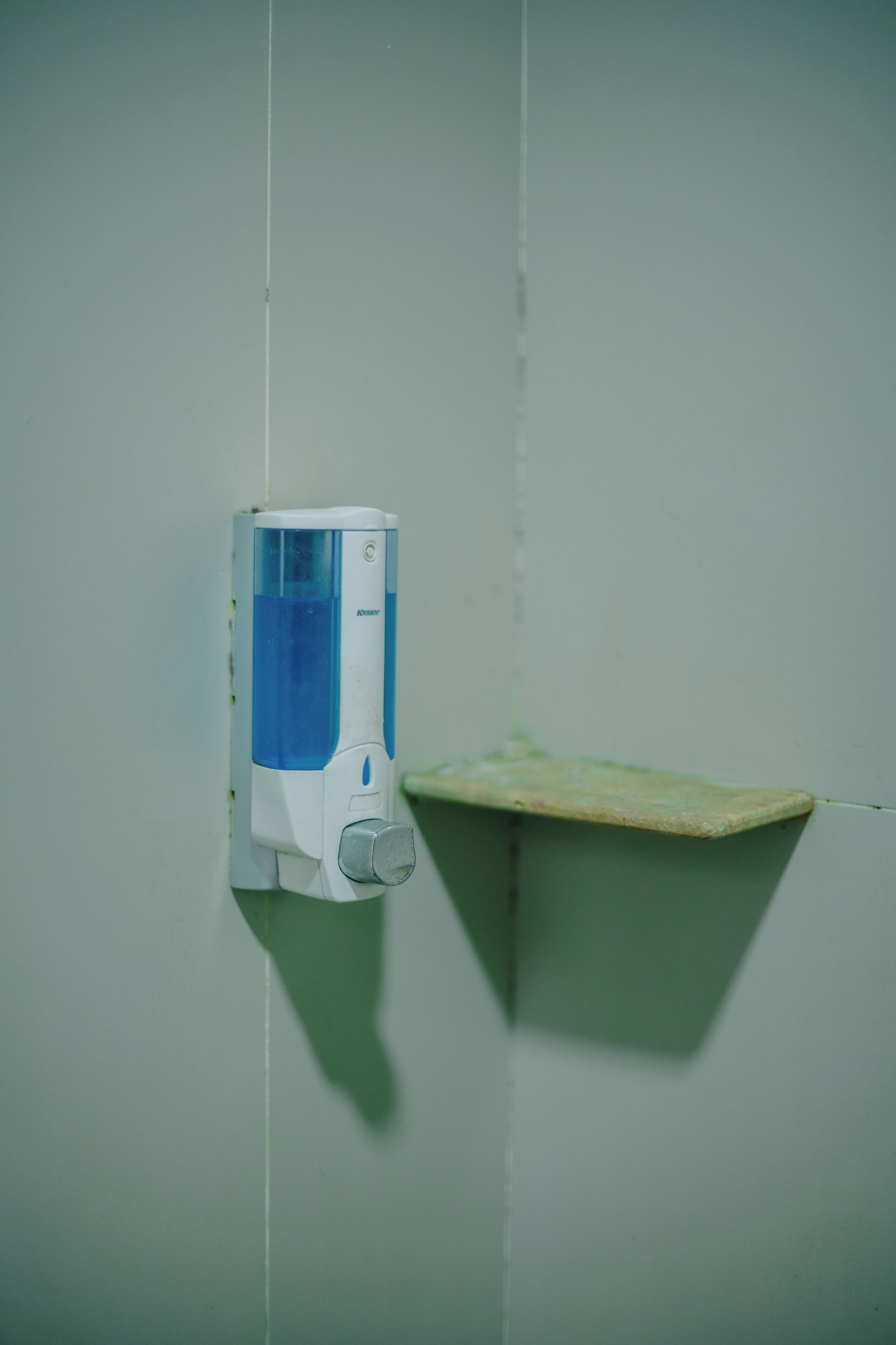 A hand soap dispenser mounted on a wall with a small shelf below it.