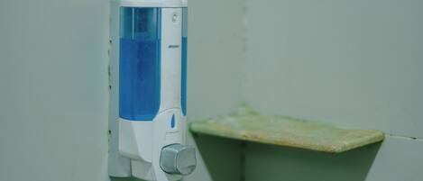 A hand soap dispenser mounted on a wall with a small shelf below it.