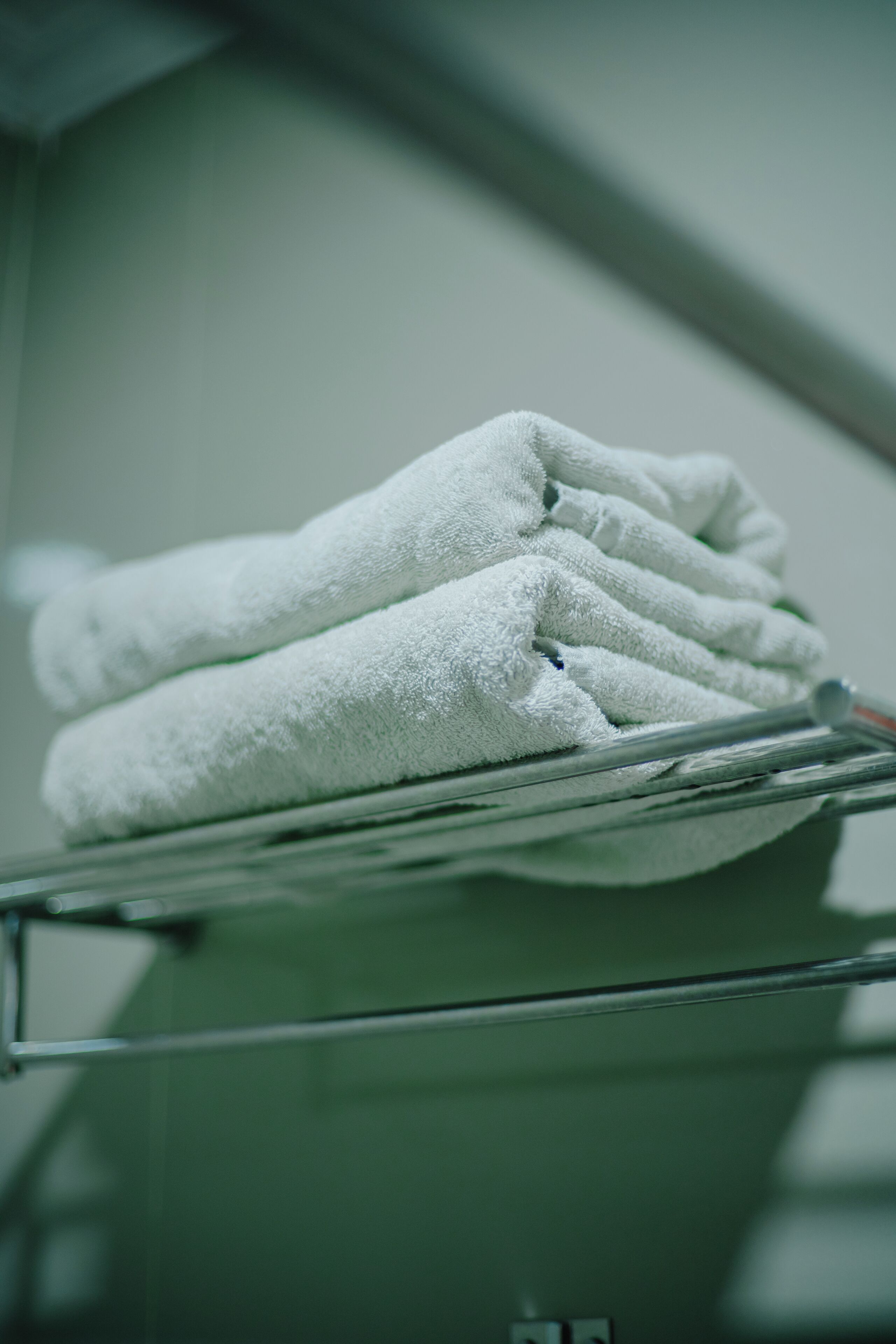A stack of white towels on a metal rack in a room with a greenish hue.