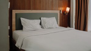 A neatly made bed with white linens and pillows, a wooden headboard, and a wall-mounted light fixture.