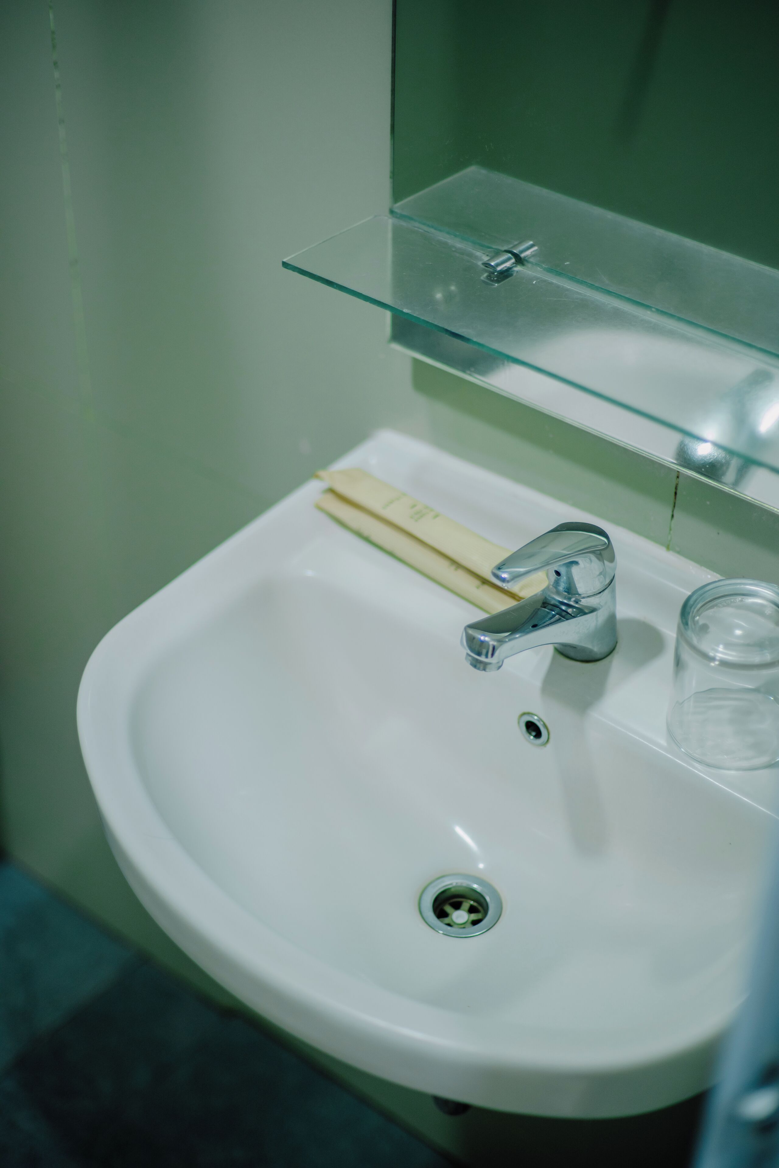 A bathroom sink with a chrome faucet, a soap bar, and a glass.