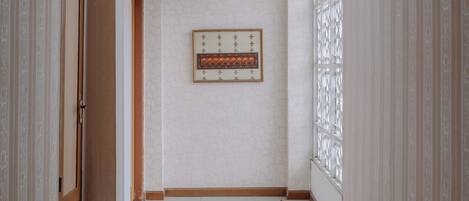 A hallway with a tiled floor, a framed artwork on the wall, and patterned wallpaper on the walls.