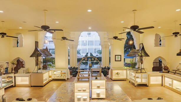 A spacious hotel lobby with a central seating area, ceiling fans, and a view of the building's exterior through large windows.