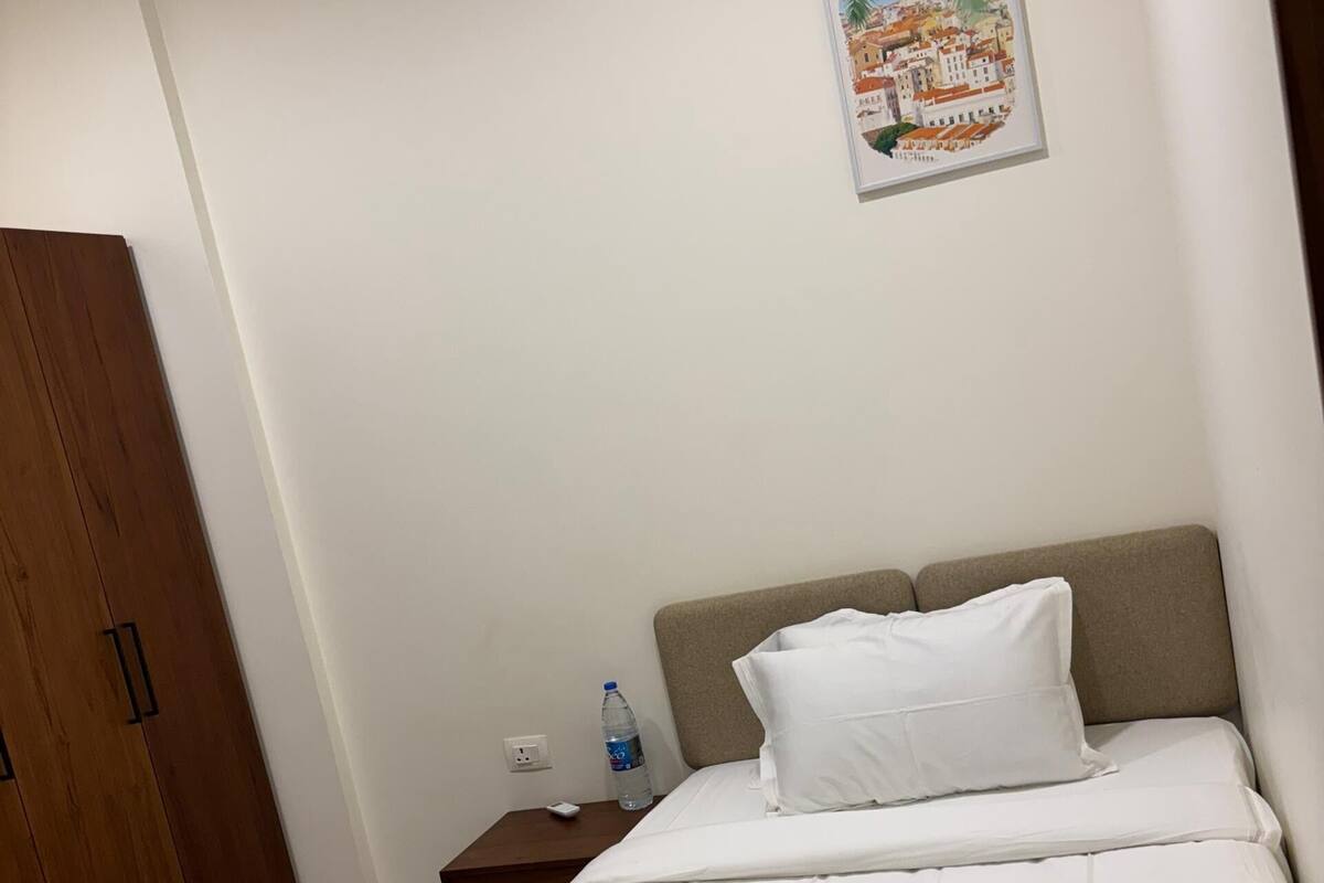 Una habitación de hotel con cama, mesita de noche, botella de agua, control remoto y armario de madera.