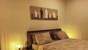 A bedroom with a bed, pillows, a nightstand, a lamp, and a painting on the wall. - Majestic Manor  (Diamniadio)