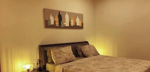 A bedroom with a bed, pillows, a nightstand, a lamp, and a painting on the wall.