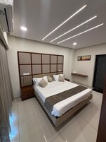 Un dormitorio moderno con una cama grande, mesitas de noche, cabecera, estante en la pared y una puerta.