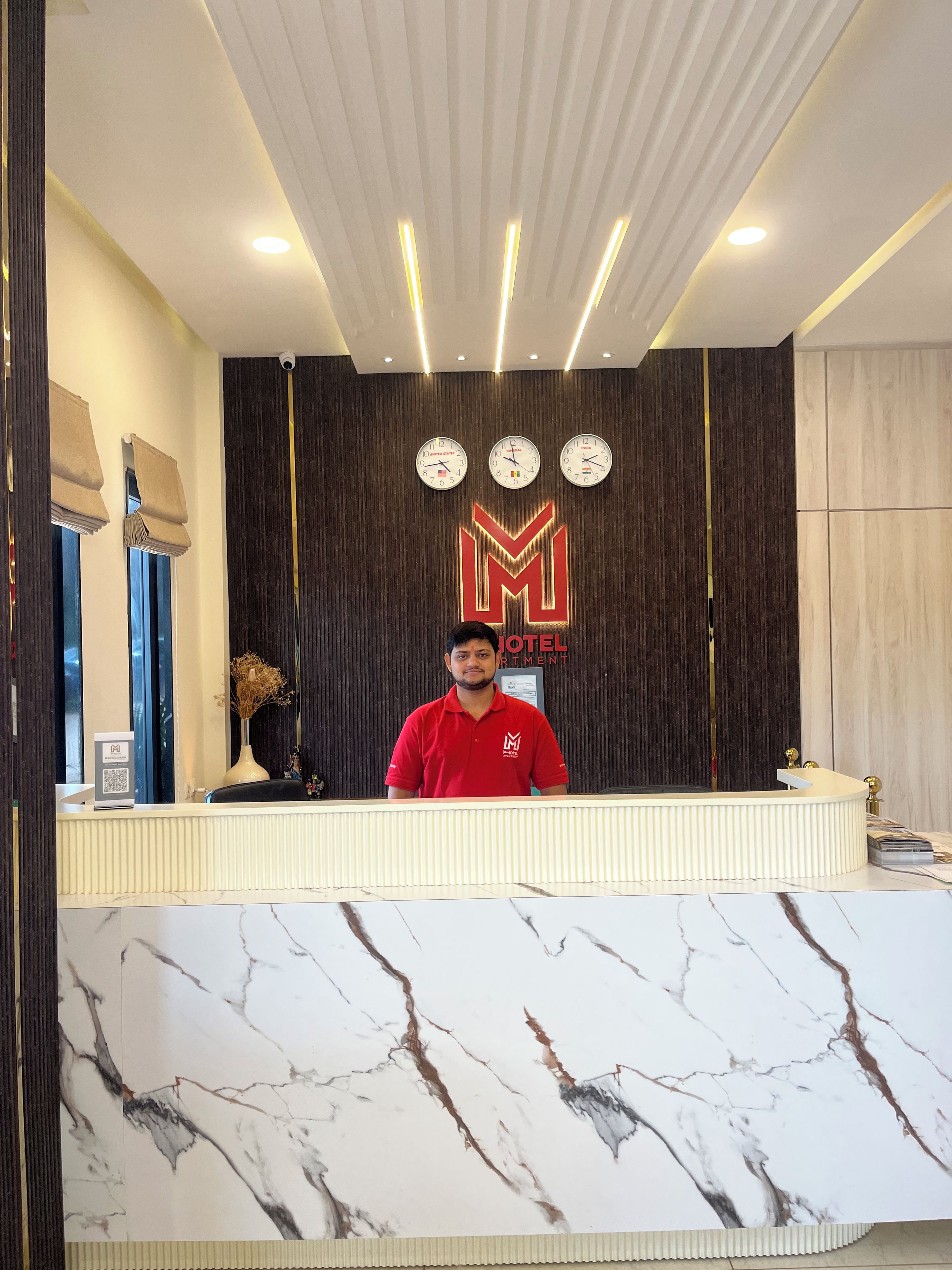 A hotel reception desk with a marble counter, a clock, and a logo on the wall.