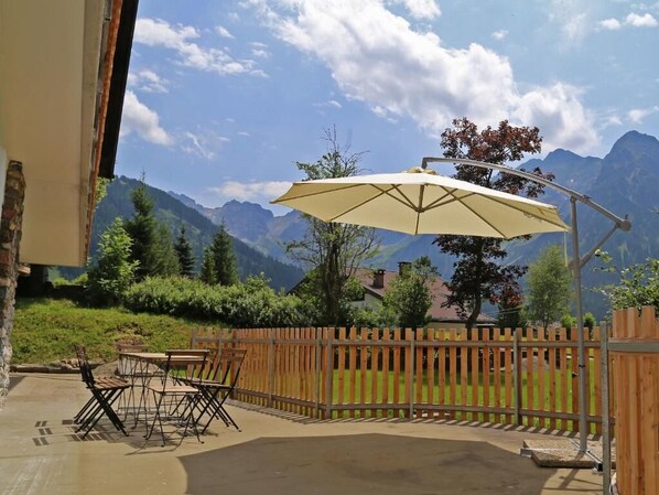 Eine Terrasse im Freien mit Holzlattenzaun, Tisch und Stühlen sowie einem großen Sonnenschirm.
