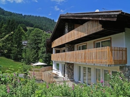 Un chalet a due piani con un balcone in legno, fondamenta in pietra e vista su una verde vallata.