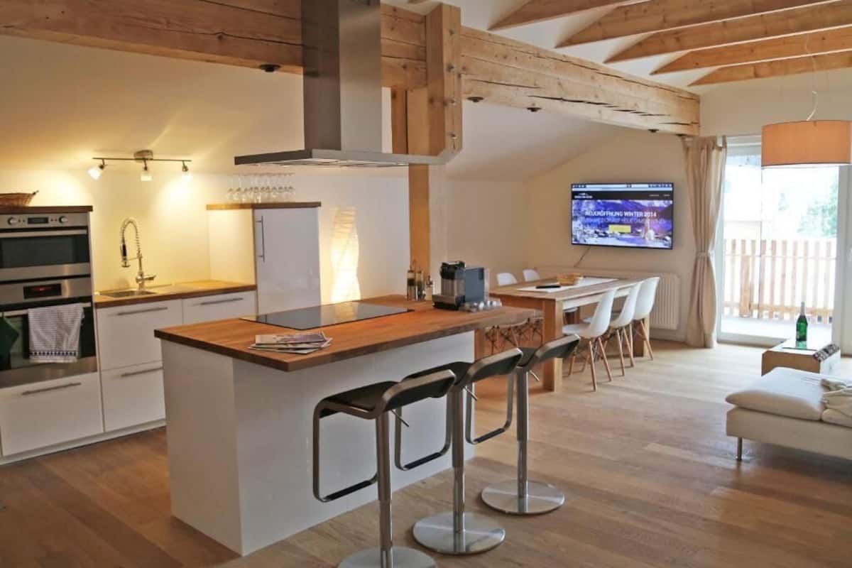 Una cocina moderna con una isla central, taburetes de bar, una zona de comedor con televisor y un rincón de descanso acogedor.