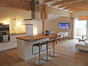 A modern kitchen with a central island, bar stools, a dining area with a TV, and a cozy seating area. - Berghaus Anna Lisa (Mittelberg)