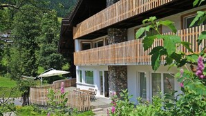 A modern chalet with a stone facade, wooden balconies, and a garden with flowers and a patio area. - Berghaus Anna Lisa (Mittelberg)