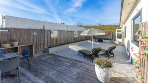Une terrasse en bois avec des meubles d’extérieur, un espace salon couvert et une cour intérieure délimitée par une clôture.