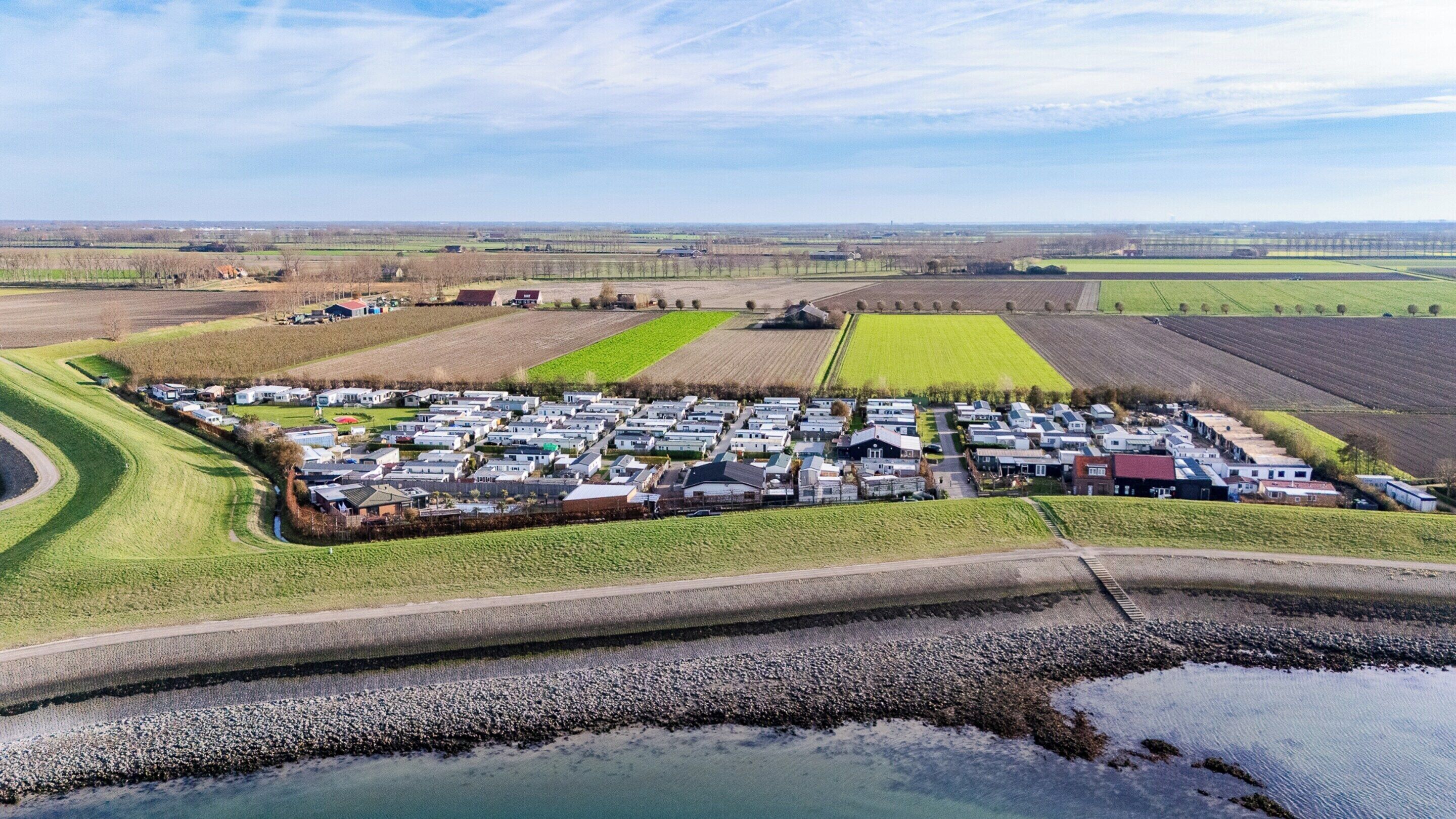 An aerial view of a caravan park with rows of caravans, a small body of water, and surrounding agricultural fields.