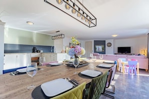A modern kitchen with white cabinets, a dining area with a wooden table set for four, and a living area with a sofa and TV. - Relaxing House With Fenced Garden (Koudekerke)