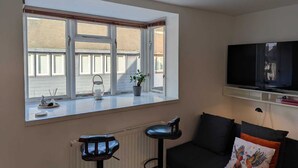 Un salon avec une grande fenêtre, un téléviseur, un canapé et deux tabourets de bar.
