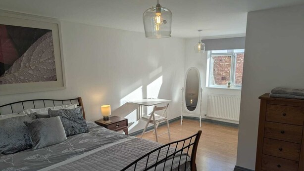 Une chambre à coucher comprenant un lit, une table de chevet, une chaise, une commode et une fenêtre donnant sur un immeuble en briques.