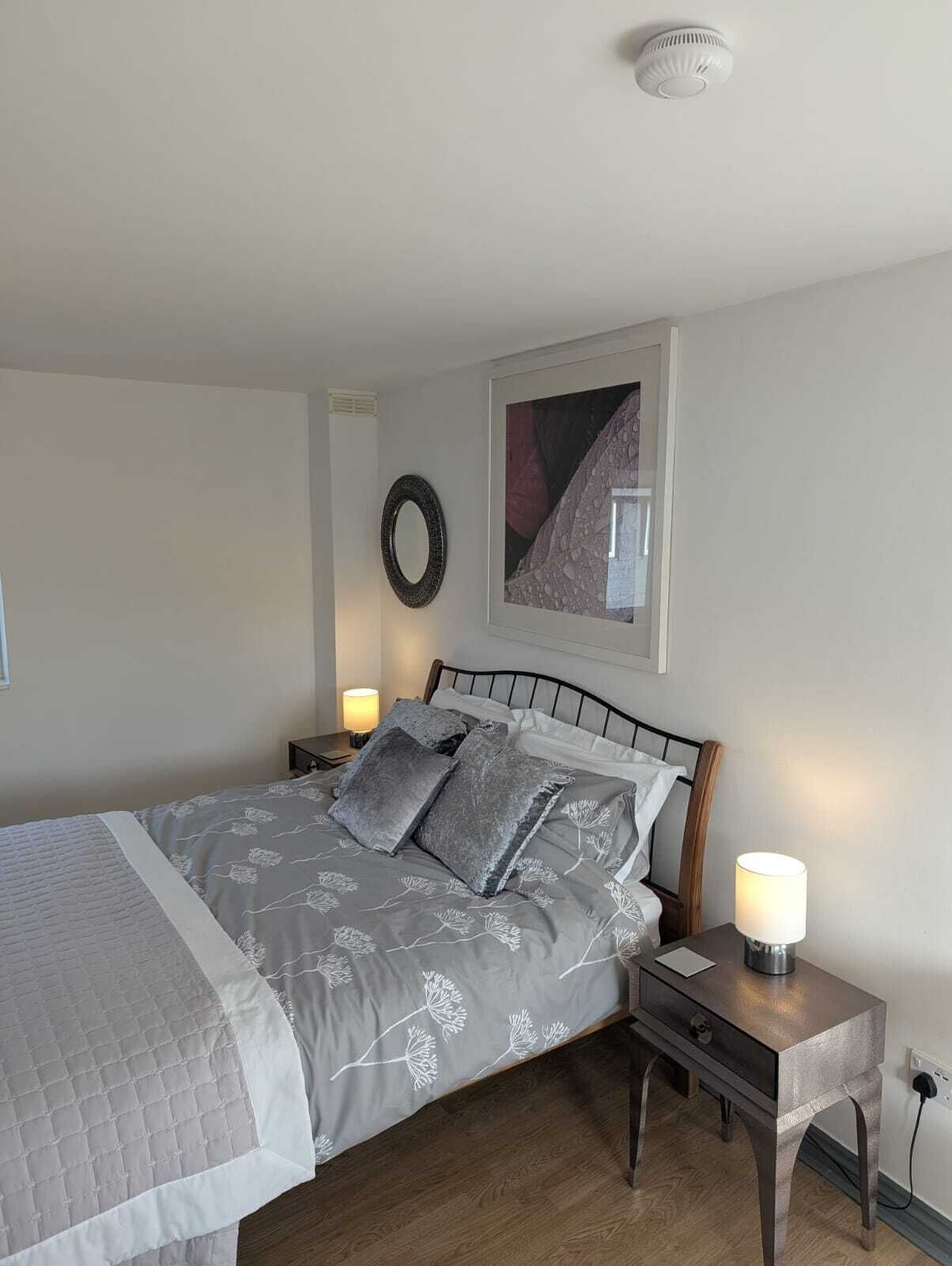 Una camera da letto ordinata con un letto, comodini, una lampada a parete e un quadro incorniciato.