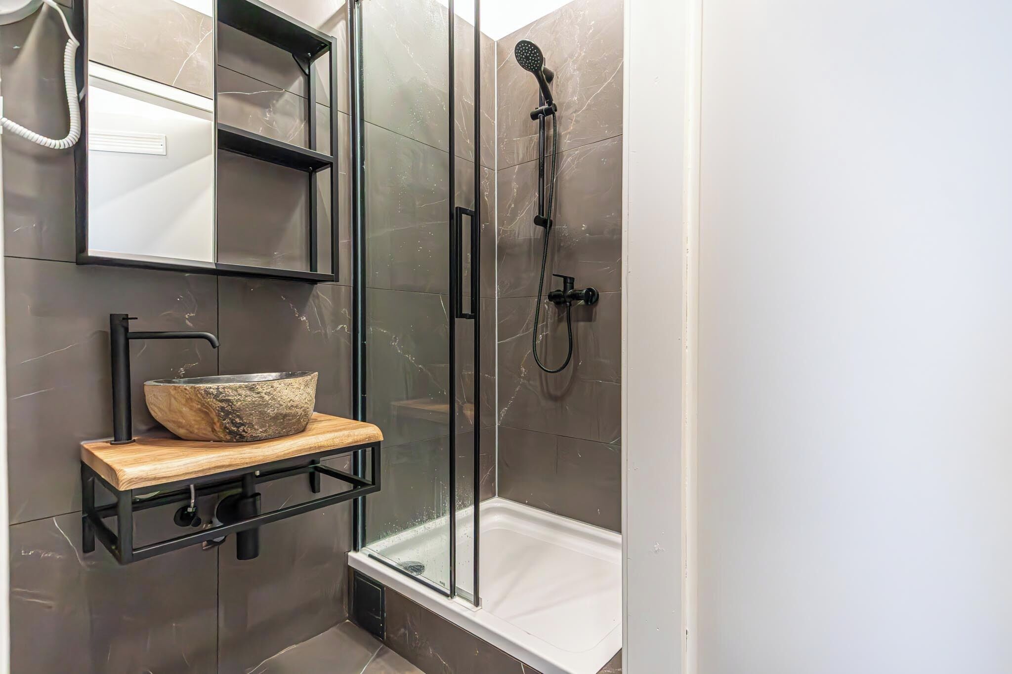 Un baño moderno con ducha cubierta de vidrio, tocador de madera con lavabo de piedra y estante de pared.