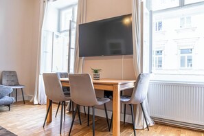 A modern living room with a wooden table, four grey chairs, a flat-screen TV, and a potted plant. - Comfortable 2BR Apt Near Attractions (Vienna)