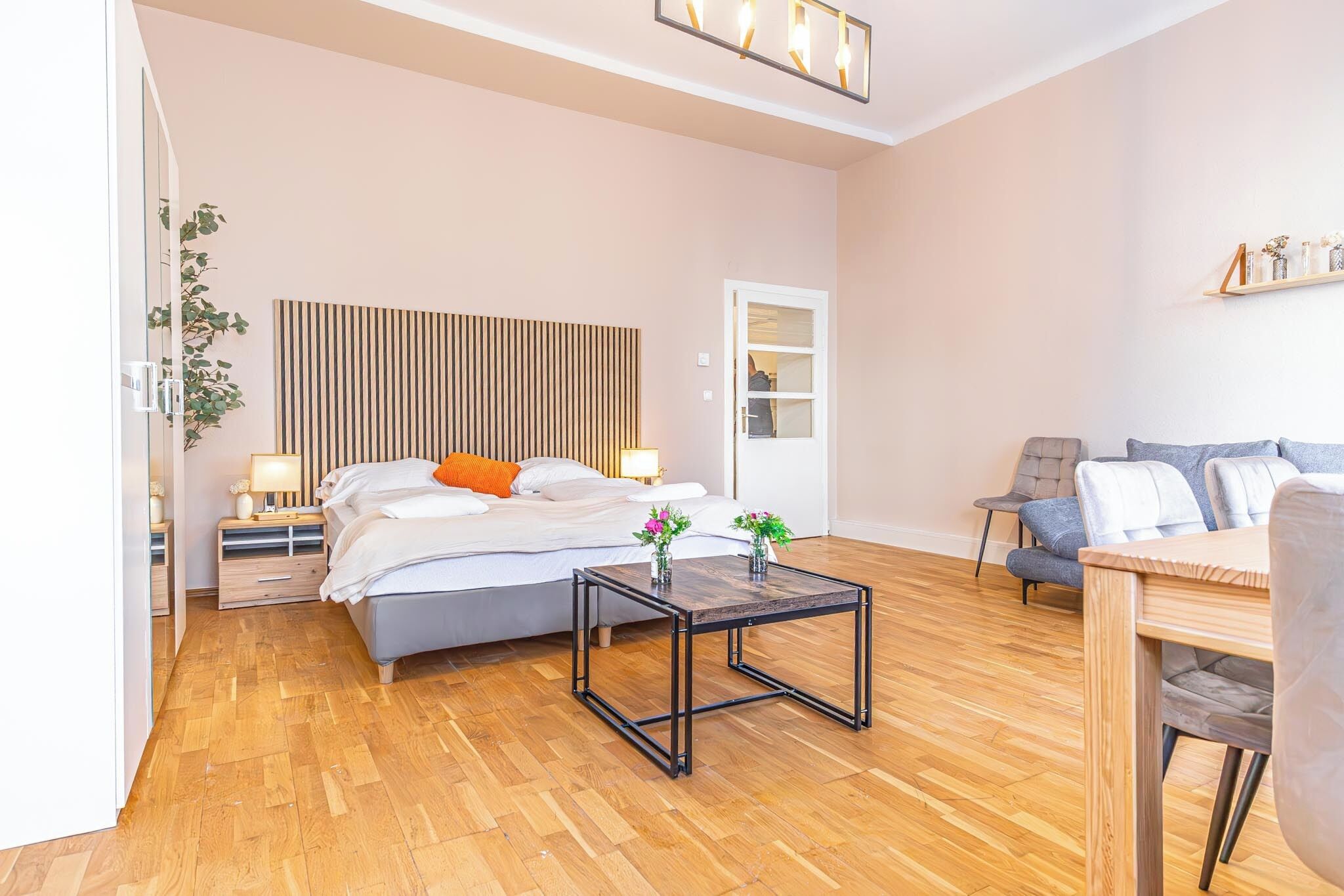 A modern bedroom with a bed, bedside tables, a wooden floor, a small table, and a sofa.