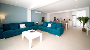 A modern living room with teal sofas, a white coffee table, and a kitchen in the background. - Vacation Villa 'Villa Esmerad' with Mountain Views, Wi-Fi and Air Conditioning (Playa Blanca)