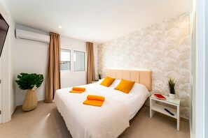 Una habitación de hotel con cama, mesita de noche, planta en maceta y ventana con cortinas.