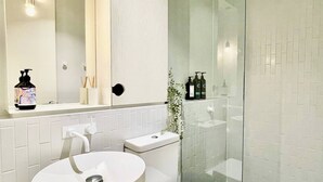 Moderni kylpyhuone, jossa on valkoinen pesuallas, wc ja lasiseinällä varustettu suihku.